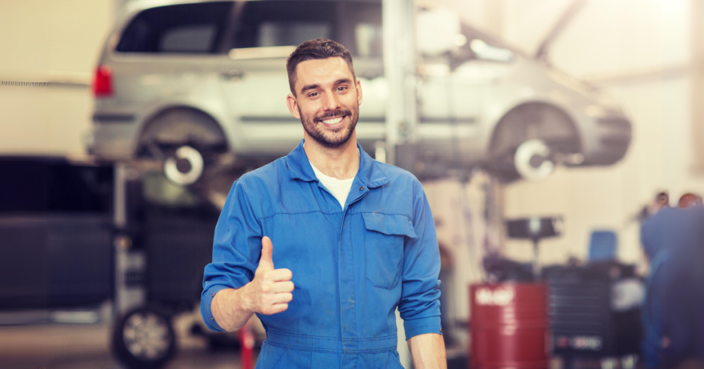 Mecânico sorrindo em oficina, destacando a importância da manutenção preventiva para motoristas de aplicativo aumentarem seus ganhos.